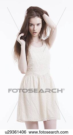 Portrait of beautiful young woman in dress with hand in her hair looking away against white background View Large Photo Image Stock Photograph - Portrait of beautiful young woman in dress with hand in her hair looking away against white background. Fotosearch