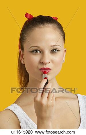 Portrait of beautiful young woman applying lipstick over yellow background View Large Photo Image Stock Image - Portrait of beautiful young woman applying lipstick over yellow background. Fotosearch