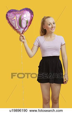 Portrait of beautiful young woman holding heart shaped birthday balloon over yellow background View Large Photo Image Stock Image - Portrait of beautiful young woman holding heart shaped birthday balloon over yellow background. Fotosearch