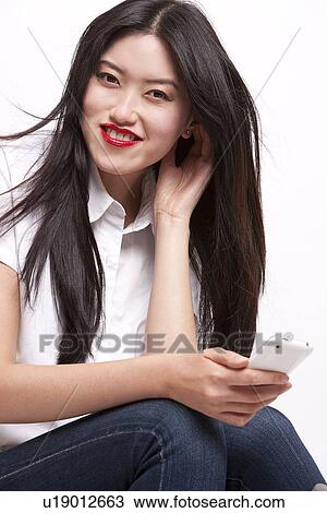 Portrait of cheerful young woman in casuals using mobile phone over white background View Large Photo Image Stock Image - Portrait of cheerful young woman in casuals using mobile phone over white background. Fotosearch