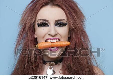 Portrait of funky young woman holding carrot in mouth over blue background View Large Photo Image Stock Photo - Portrait of funky young woman holding carrot in mouth over blue background. Fotosearch