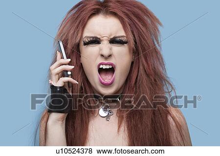 Portrait of funky young woman screaming while using cell phone over blue background View Large Photo Image Stock Photo - Portrait of funky young woman screaming while using cell phone over blue background. Fotosearch