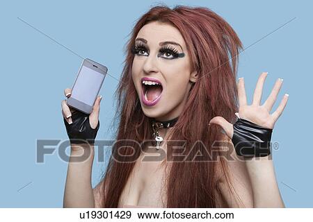 Portrait of funky young woman screaming while using cell phone over blue background View Large Photo Image Stock Photo - Portrait of funky young woman screaming while using cell phone over blue background. Fotosearch