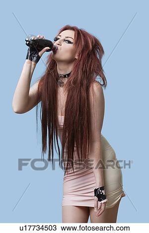Portrait of funky young woman with bottle of drink over blue background View Large Photo Image Stock Image - Portrait of funky young woman with bottle of drink over blue background. Fotosearch