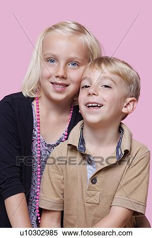 Stock Photography - Portrait of happy young boy with sister over pink background. Fotosearch