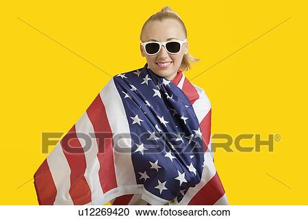Portrait of happy young woman wrapped in American flag over yellow background View Large Photo Image Stock Image - Portrait of happy young woman wrapped in American flag over yellow background. Fotosearch