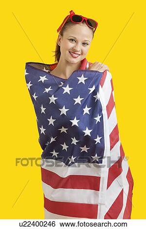 Portrait of happy young woman wrapped in American flag over yellow background View Large Photo Image Stock Photograph - Portrait of happy young woman wrapped in American flag over yellow background. Fotosearch