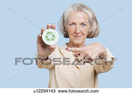 Portrait of senior woman holding badge with recycling symbol against blue background View Large Photo Image Stock Image - Portrait of senior woman holding badge with recycling symbol against blue background. Fotosearch