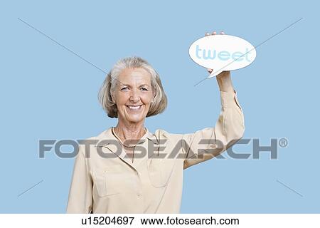 Stock Photo - Portrait of senior woman holding tweet bubble against blue background. Fotosearch
