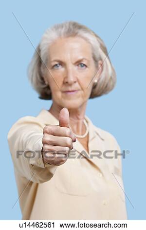 Portrait of senior woman in casuals gesturing thumbs up against blue background View Large Photo Image Stock Image - Portrait of senior woman in casuals gesturing thumbs up against blue background. Fotosearch