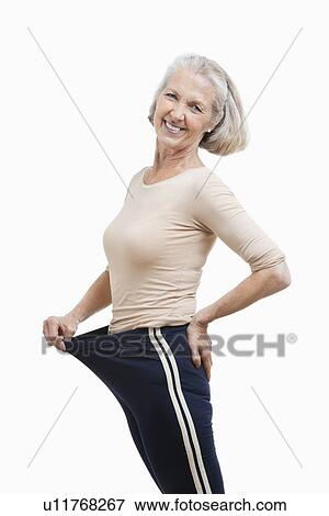 Stock Photo - Portrait of senior woman in oversized pants against white background. Fotosearch