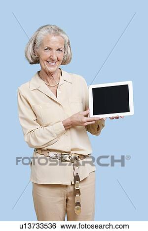 Stock Photograph - Portrait of senior woman showing tablet PC against blue background. Fotosearch
