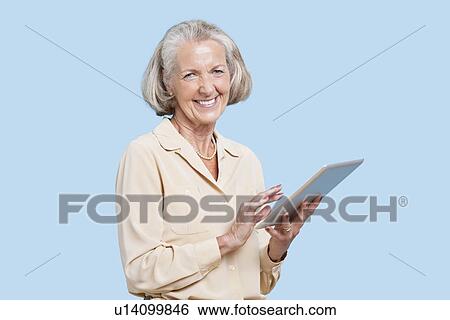 Portrait of senior woman using tablet PC against blue background View Large Photo Image Stock Photograph - Portrait of senior woman using tablet PC against blue background. Fotosearch