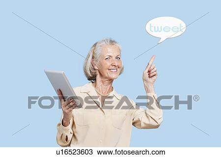 Portrait of senior woman with tablet PC pointing at tweet bubble against blue background View Large Photo Image Stock Image - Portrait of senior woman with tablet PC pointing at tweet bubble against blue background. Fotosearch
