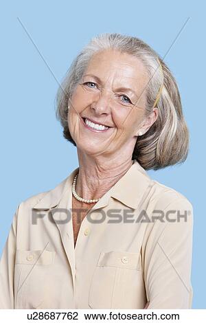 Stock Image - Portrait of smiling senior woman in casuals against blue background. Fotosearch