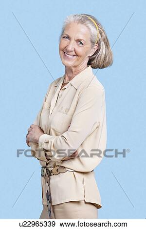 Portrait of smiling senior woman in casuals with arms crossed against blue background View Large Photo Image Stock Photo - Portrait of smiling senior woman in casuals with arms crossed against blue background. Fotosearch