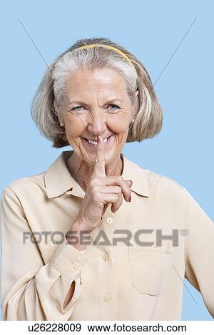 Portrait of smiling senior woman in casuals with finger on lips against blue background View Large Photo Image Stock Photo - Portrait of smiling senior woman in casuals with finger on lips against blue background. Fotosearch