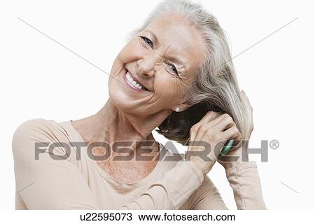 Portrait of smiling senior woman combing her hair against white background View Large Photo Image Stock Image - Portrait of smiling senior woman combing her hair against white background. Fotosearch