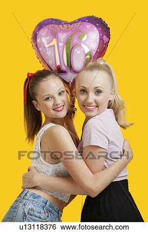 Portrait of two happy young women with birthday balloon hugging over yellow background View Large Photo Image Stock Photograph - Portrait of two happy young women with birthday balloon hugging over yellow background. Fotosearch