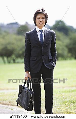 Portrait of young businessman carrying briefcase standing at park View Large Photo Image Picture - Portrait of young businessman carrying briefcase standing at park. Fotosearch
