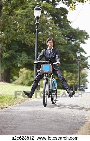 Portrait of young businessman riding bicycle with legs kicked out View Large Photo Image Stock Image - Portrait of young businessman riding bicycle with legs kicked out. Fotosearch