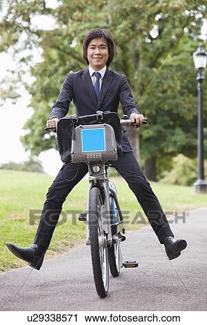 Stock Image - Portrait of young businessman riding bicycle with apart. Fotosearch