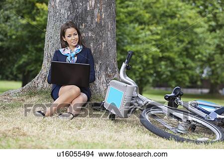 Portrait of young businesswoman with laptop and bicycle sitting at park View Large Photo Image Picture - Portrait of young businesswoman with laptop and bicycle sitting at park. Fotosearch