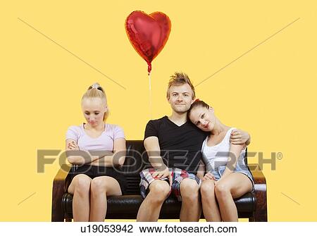 Portrait of young couple sitting on sofa with female friend feeling left out over yellow background View Large Photo Image Stock Image - Portrait of young couple sitting on sofa with female friend feeling left out over yellow background. Fotosearch
