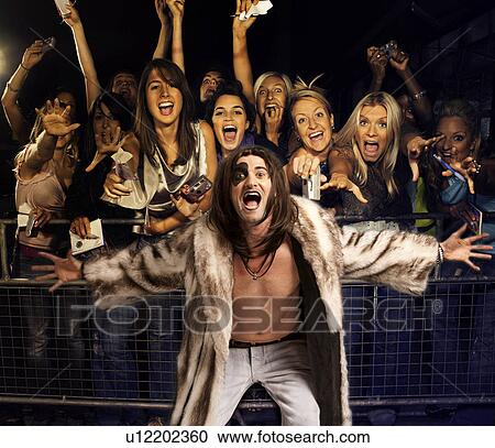 Stock Image - Portrait of young man in fur coat screaming with excited audience in the background. Fotosearch