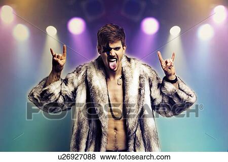 Stock Photo - Portrait of young man in fur coat making rebellious hand gestures in rock concert. Fotosearch