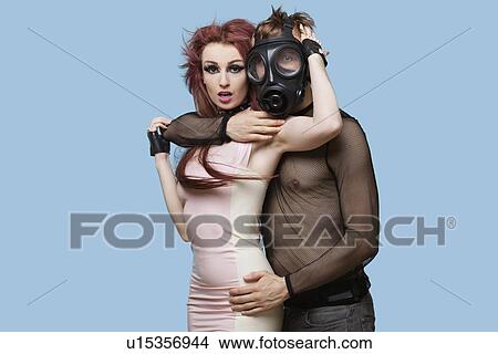 Portrait of young man wearing gas mask embraces funky woman over blue background View Large Photo Image Picture - Portrait of young man wearing gas mask embraces funky woman over blue background. Fotosearch