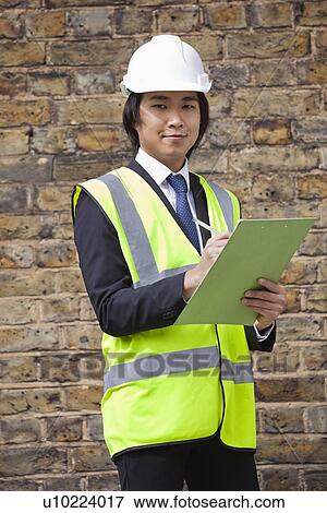 Stock Photo - Portrait of young supervisor holding clipboard at construction site. Fotosearch