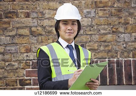 Portrait of young supervisor holding clipboard at construction site View Large Photo Image Stock Photo - Portrait of young supervisor holding clipboard at construction site. Fotosearch