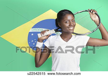 Stock Photography - Portrait of young woman with tennis racket against Brazilian flag. Fotosearch