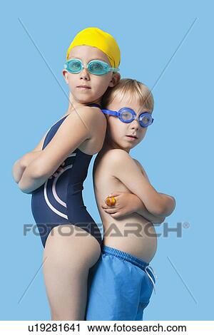 Stock Image - Profile shot of young boy and girl in swimwear standing back to back over blue background. Fotosearch