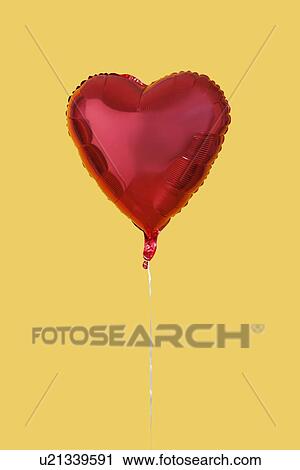 Stock Image - Red heart shaped balloon over yellow background. Fotosearch