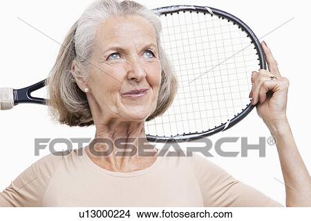 Senior woman holding tennis racket over her shoulder against white background View Large Photo Image Picture - Senior woman holding tennis racket over her shoulder against white background. Fotosearch