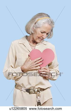 Senior woman in casuals holding red paper heart against blue background View Large Photo Image Stock Photography - Senior woman in casuals holding red paper heart against blue background. Fotosearch