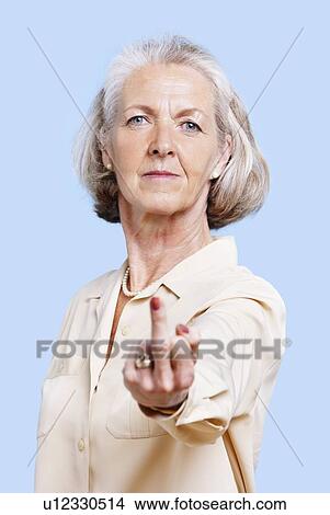 Senior woman in casuals making rebellious hand gesture against blue background View Large Photo Image Picture - Senior woman in casuals making rebellious hand gesture against blue background. Fotosearch