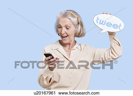 Stock Image - Senior woman in casuals using social media on her Smartphone against blue background. Fotosearch