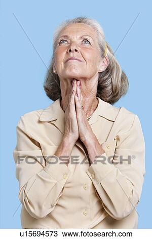 Senior woman praying with hands clasped against blue background View Large Photo Image Stock Image - Senior woman praying with hands clasped against blue background. Fotosearch