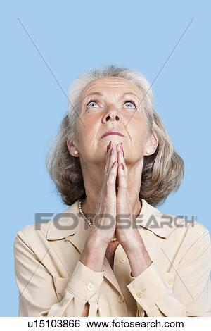 Senior woman praying with hands clasped against blue background View Large Photo Image Stock Photograph - Senior woman praying with hands clasped against blue background. Fotosearch