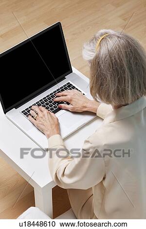 Stock Image - Senior woman surfing the net on laptop at home. Fotosearch