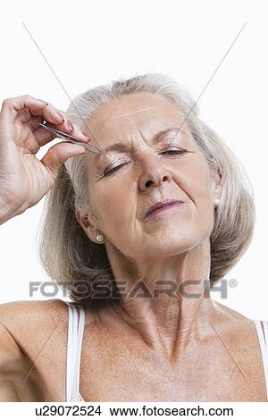 Picture - Senior woman tweezing eyebrows against white background. Fotosearch