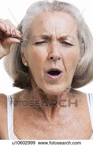 Senior woman tweezing eyebrows against white background View Large Photo Image Stock Photo - Senior woman tweezing eyebrows against white background. Fotosearch