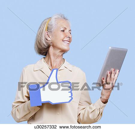 Senior woman with tablet PC holding fake like button against blue background View Large Photo Image Stock Image - Senior woman with tablet PC holding fake like button against blue background. Fotosearch
