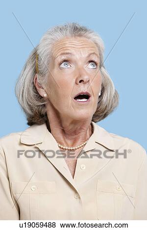 Stock Photo - Shocked senior woman in casuals looking away against blue background. Fotosearch