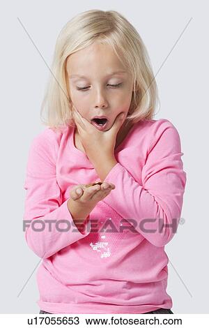 Stock Image - Shocked young girl holding coins over white background. Fotosearch