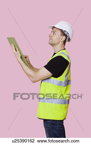 Side view of a male construction worker with clipboard looking away over pink background View Large Photo Image Stock Image - Side view of a male construction worker with clipboard looking away over pink background. Fotosearch