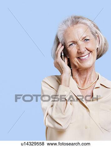 Smiling senior woman using cell phone against blue background View Large Photo Image Stock Photo - Smiling senior woman using cell phone against blue background. Fotosearch